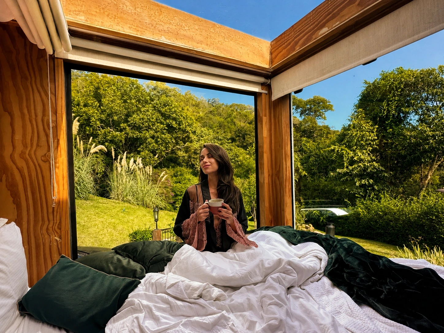 Mulher sentada na cama da Sky Cabin con teto de vidro aberto durante o dia